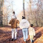 A family of four strolling on a leaf-covered path in a fall forest.