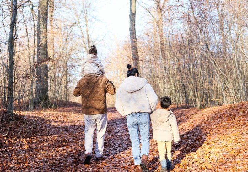 A family of four strolling on a leaf-covered path in a fall forest.
