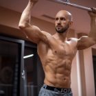 A bald, muscular man performing exercise on gym equipment indoors.