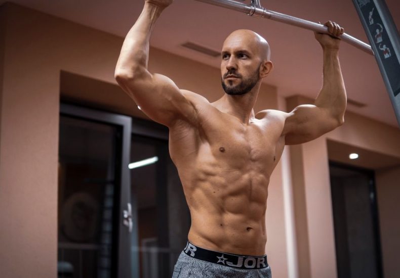 A bald, muscular man performing exercise on gym equipment indoors.
